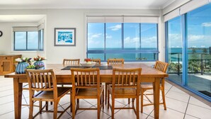 A dining area with a wooden table and chairs, a bowl of fruit, and a framed picture on the wall. - Alexandra on the Pacific (Alexandra Headland)