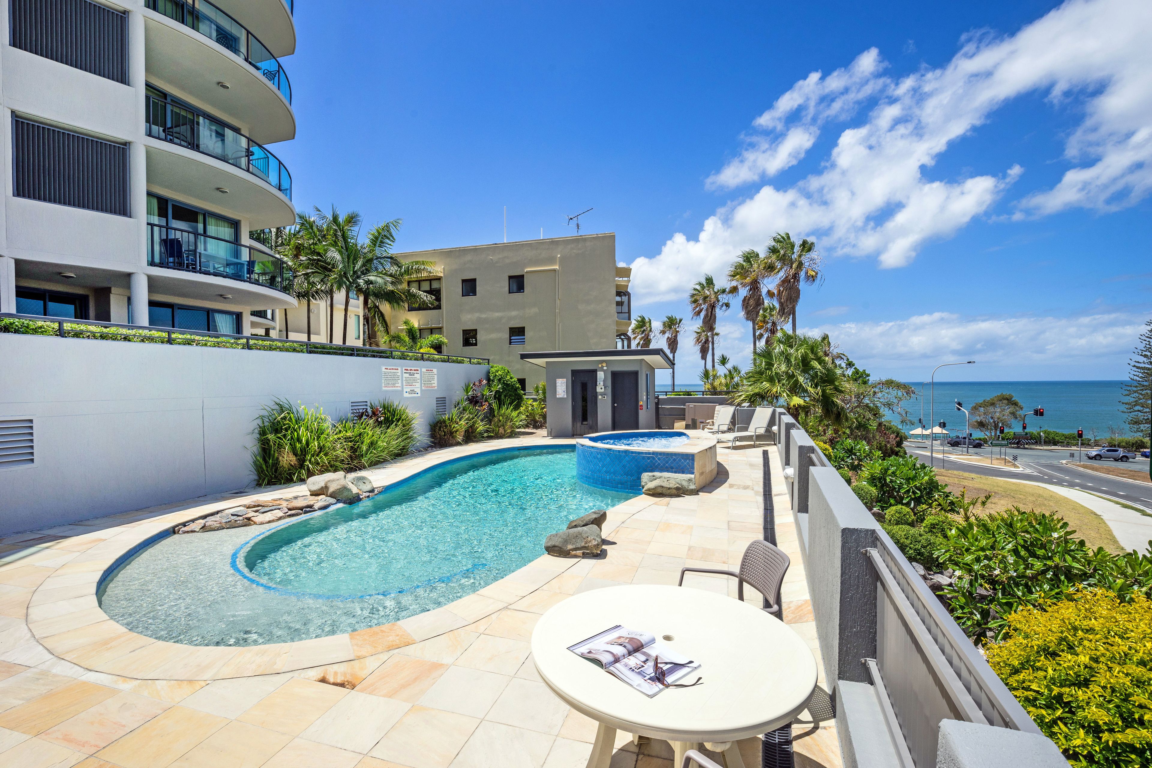 A modern hotel with a pool, outdoor seating, and a view of the ocean.