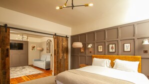 A bedroom with a large bed, a wooden headboard, a TV, a sofa, and a sliding door leading to another room. - The West Bay Hotel (Bridport)