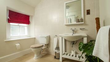 A bathroom with a toilet, sink, mirror, and a window with a red valance.