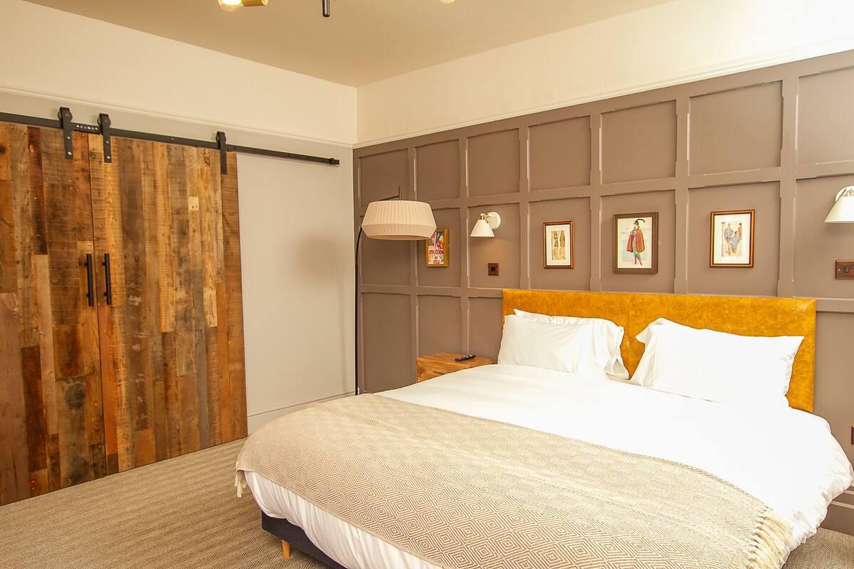 A bedroom with a large bed, wooden wardrobe, and a headboard with framed pictures.