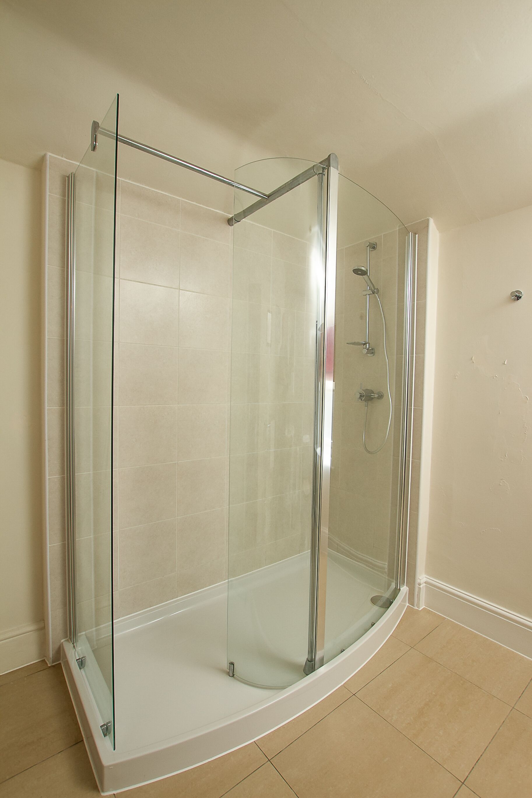 A glass-enclosed shower stall with a curved design, a handheld showerhead, and a wall-mounted faucet.