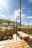 Una terraza de madera con bancos, un muro de piedra y vistas a una zona residencial con casas y coches aparcados.