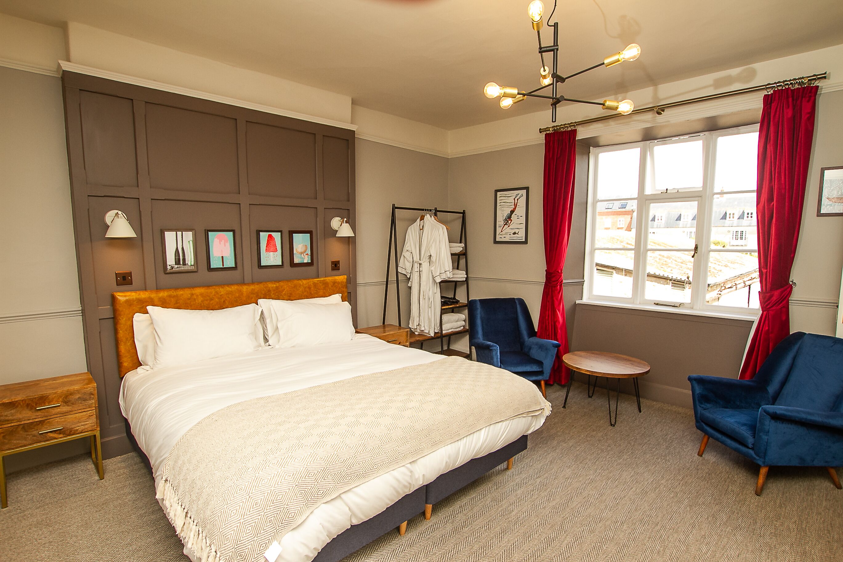 A hotel room with a large bed, a bedside table, a chair, a small table, and a window with curtains.