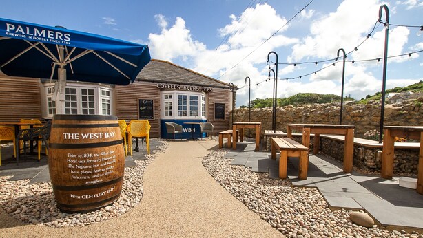 A wooden building with a sign reading "COFFEE BEERS ICES" and "THE WEST BAY". - The West Bay Hotel (Bridport)