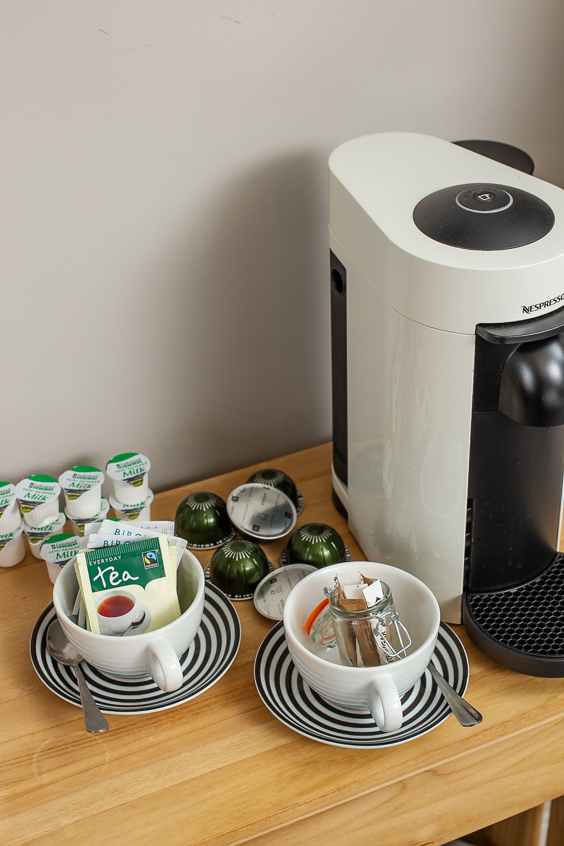 A coffee maker, two cups with tea bags, and a bottle of milk on a wooden table.