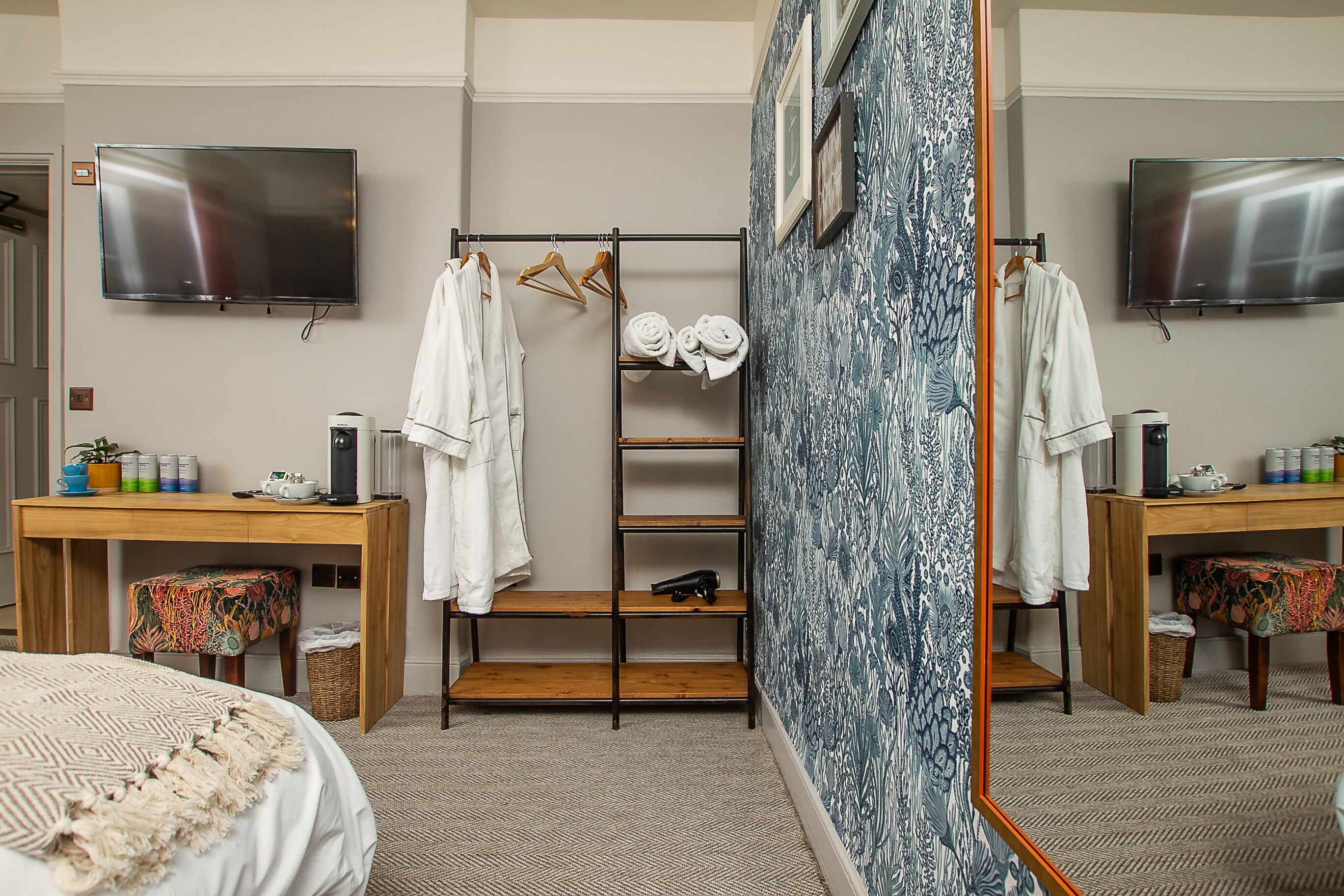A hotel room with a bed, a wooden desk, a shelf with towels, a television, and a wardrobe.