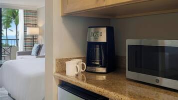 Une cuisine d’hôtel équipée d’une machine à café et d’un four à micro-ondes, ainsi qu’une chambre avec un lit donnant sur des palmiers.