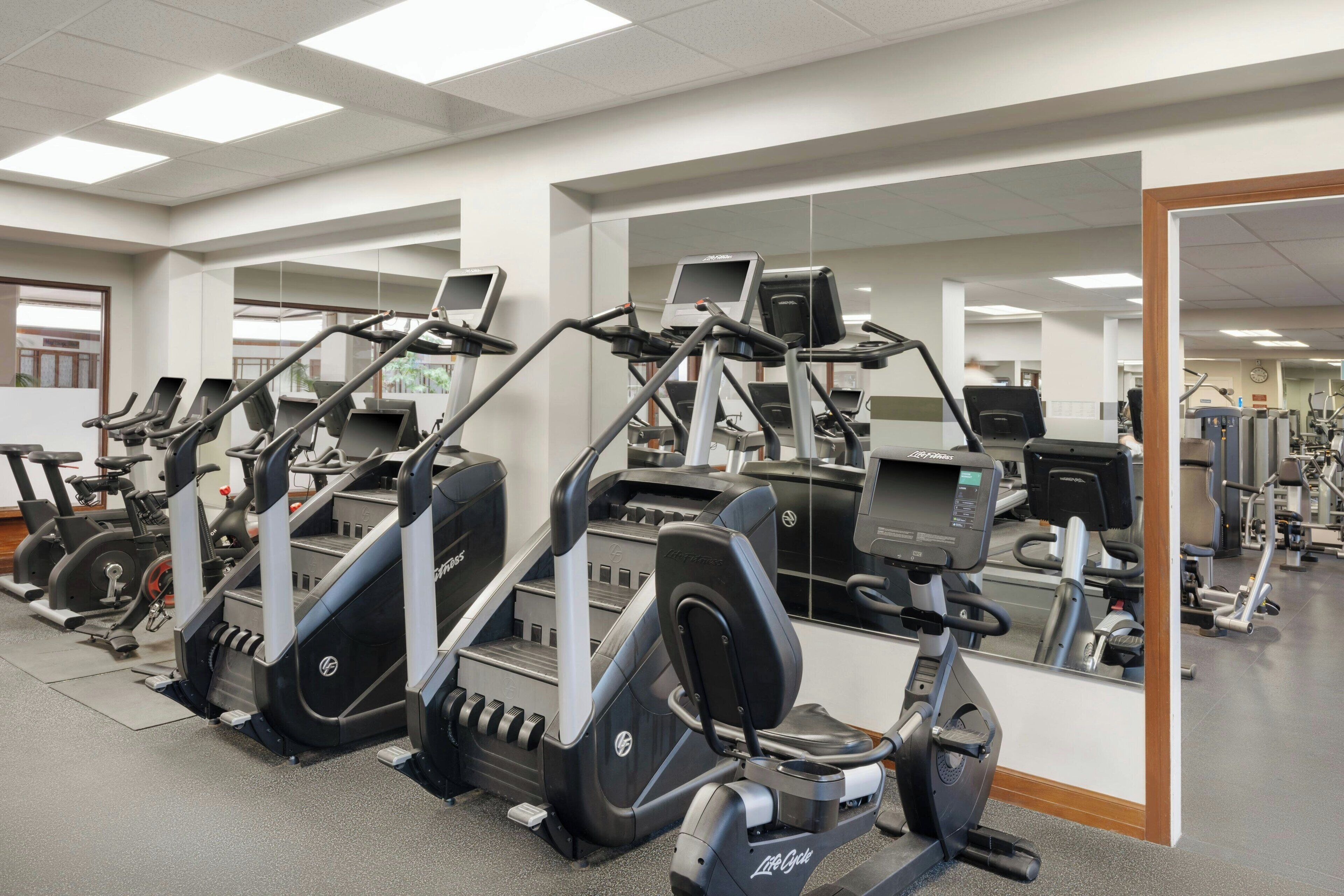 A gym with multiple cardio machines, mirrors, and exercise equipment.