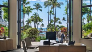 A modern office with a desk, computer, and chair, overlooking a pool and palm trees.