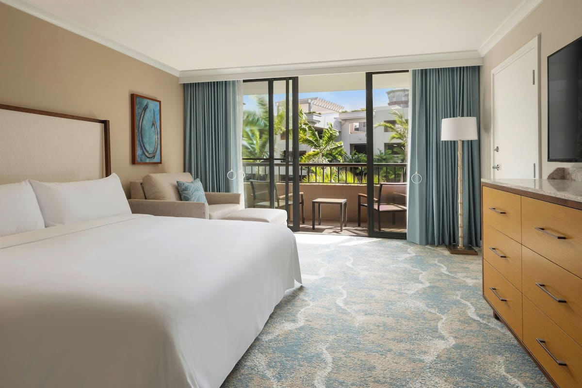 A hotel room with a large bed, a sofa, a dining area with a table and chairs, a TV, and a balcony with curtains.