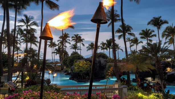 A resort with a pool, palm trees, and a night scene with fire torches.