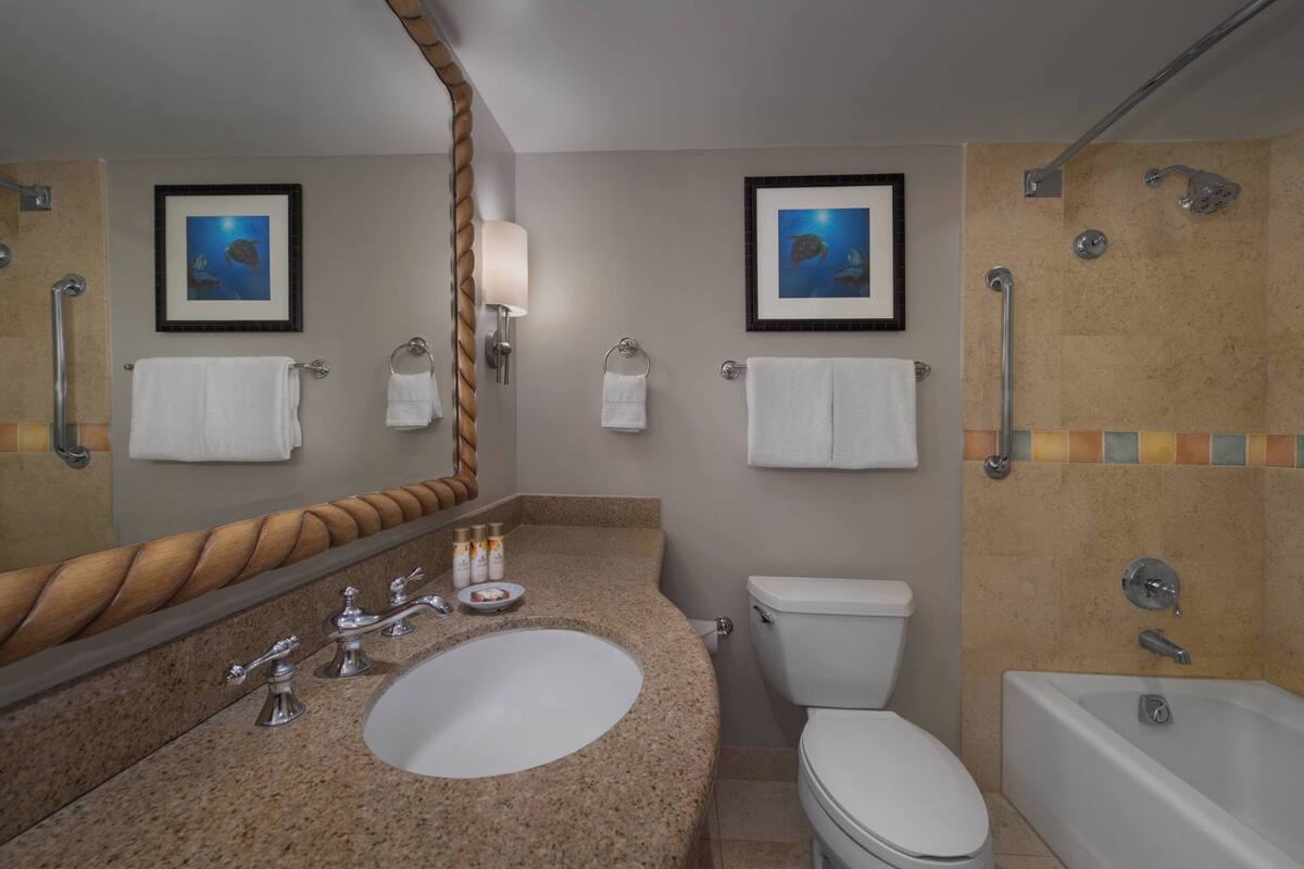 Een badkamer met een wastafel, toilet en bad. Er hangen prestaties aan de muur, een handdoekrek en een spiegel met houten lijst.