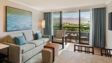 A hotel room with a balcony, a sofa, a chair, a table, and a painting on the wall.