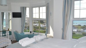 Una camera d'albergo con un letto grande, vista sul mare, televisione e finestra con tende.