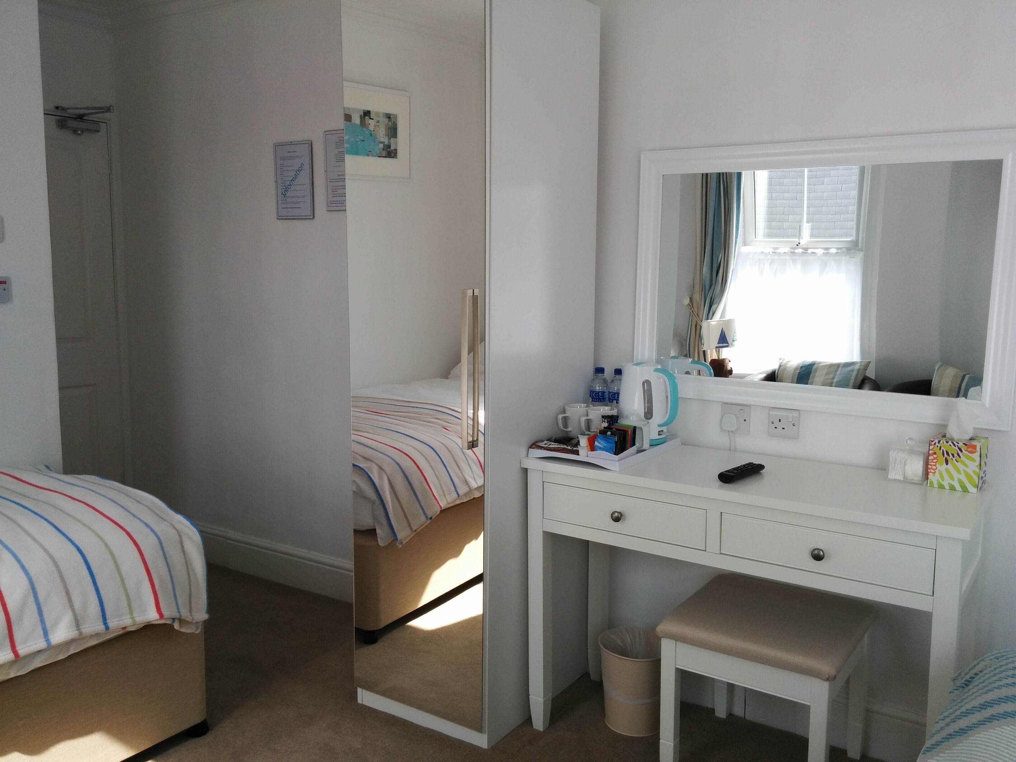 Un dormitorio con cama, una mesita de noche con espejo, un escritorio con silla y una ventana con cortinas.
