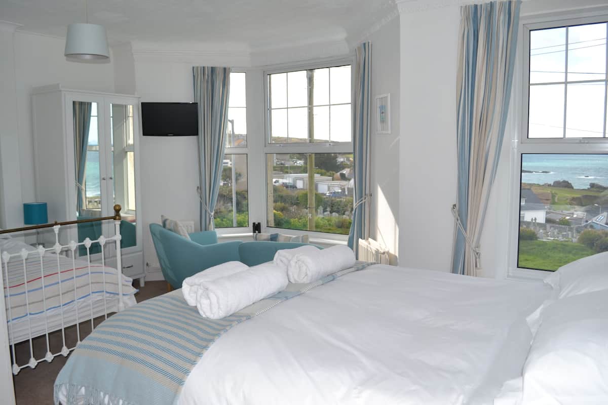 A bedroom with a large bed, a window with a view, a TV, and a wardrobe.