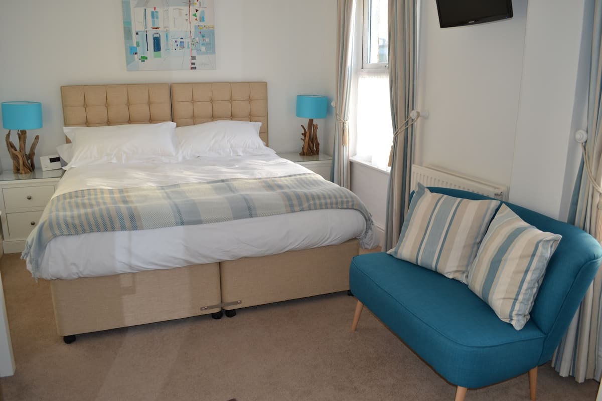 A bedroom with a bed, a blue sofa, a nightstand, a lamp, and a wall-mounted TV.