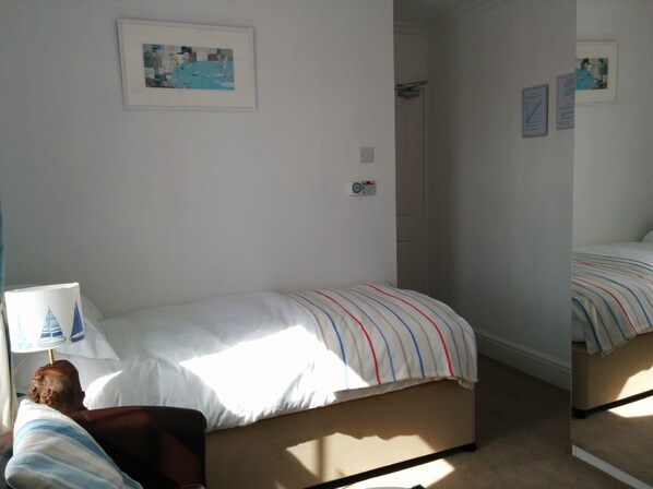 A bedroom with a bed, a chair, a lamp, and a wall-mounted picture. - Tregony Guest House (St Ives)