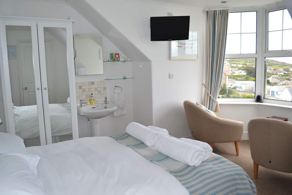 A hotel room with a bed, a chair, a TV, a sink, and a window with a view.