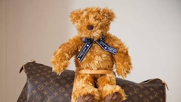 Un oso de peluche sentado sobre un bolso deportivo Louis Vuitton, sobre una maleta plateada de Samsonite.