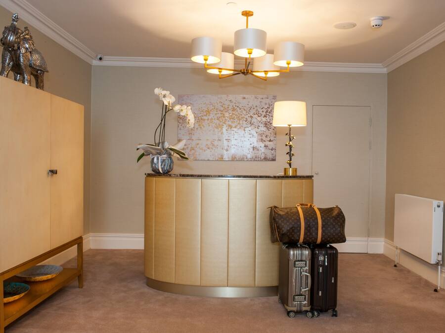 Un espace d’accueil doté d’un comptoir d’accueil incurvé, d’un lustre, d’un grand tableau abstrait, d’une lampe et d’un présentoir à bagages avec une valise et un sac Louis Vuitton.