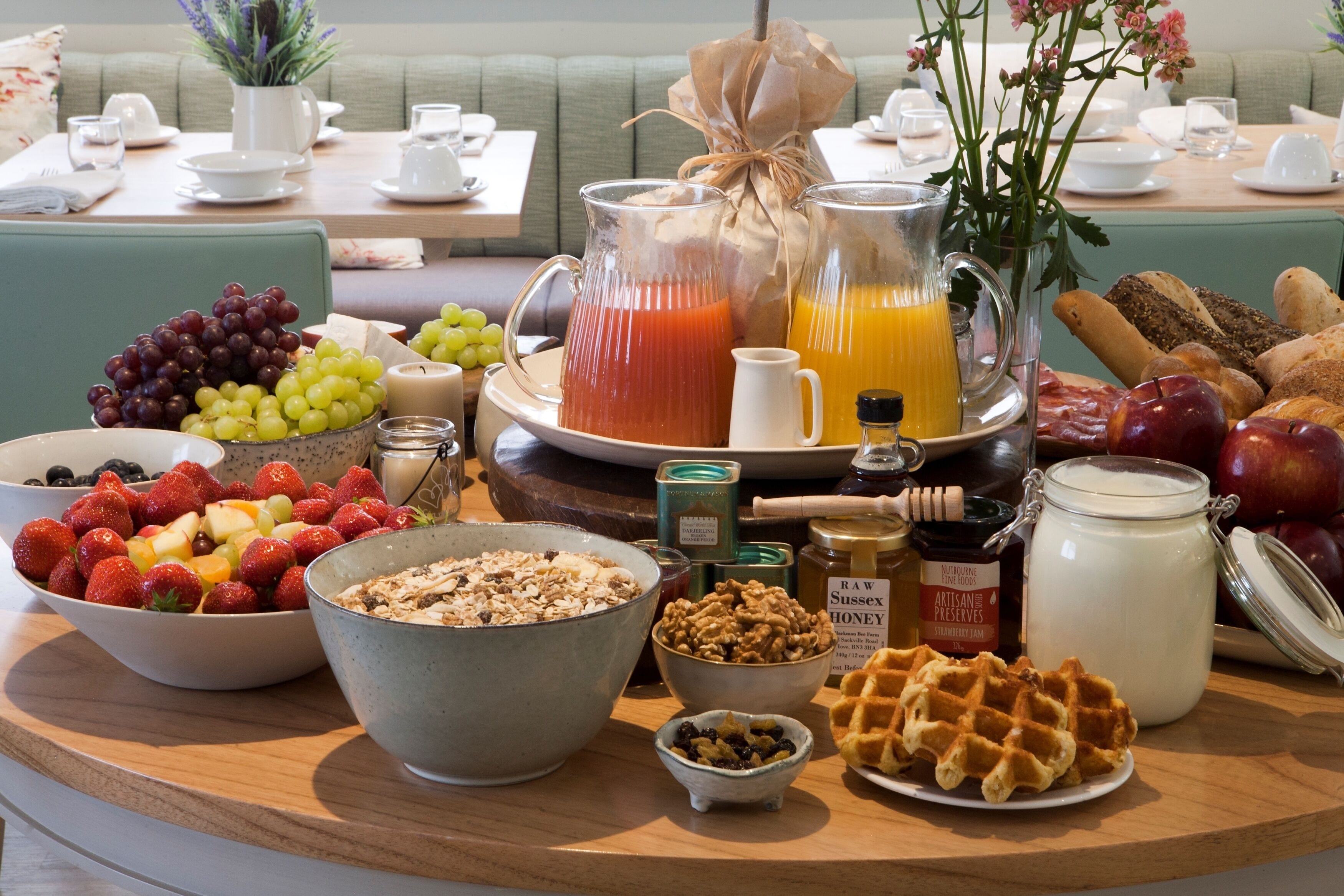 A breakfast buffet with various fruits, cereals, honey, and a waffle.