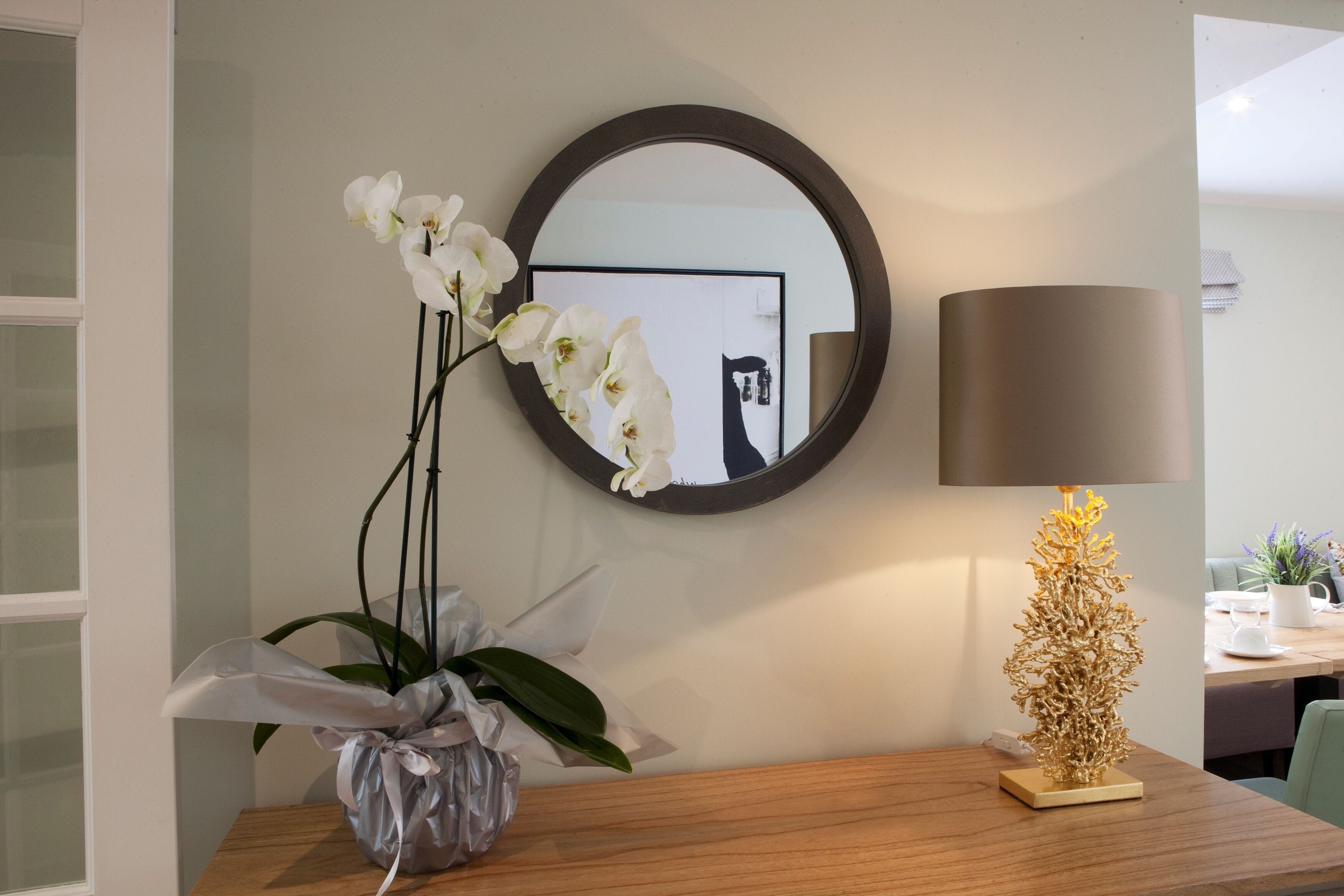 Une pièce avec une table en bois, un miroir, une lampe et un vase contenant des orchidées.