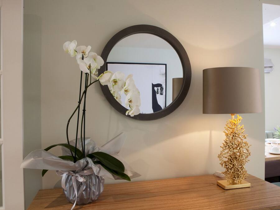 A room with a wooden table, a mirror, a lamp, and a vase with orchids.