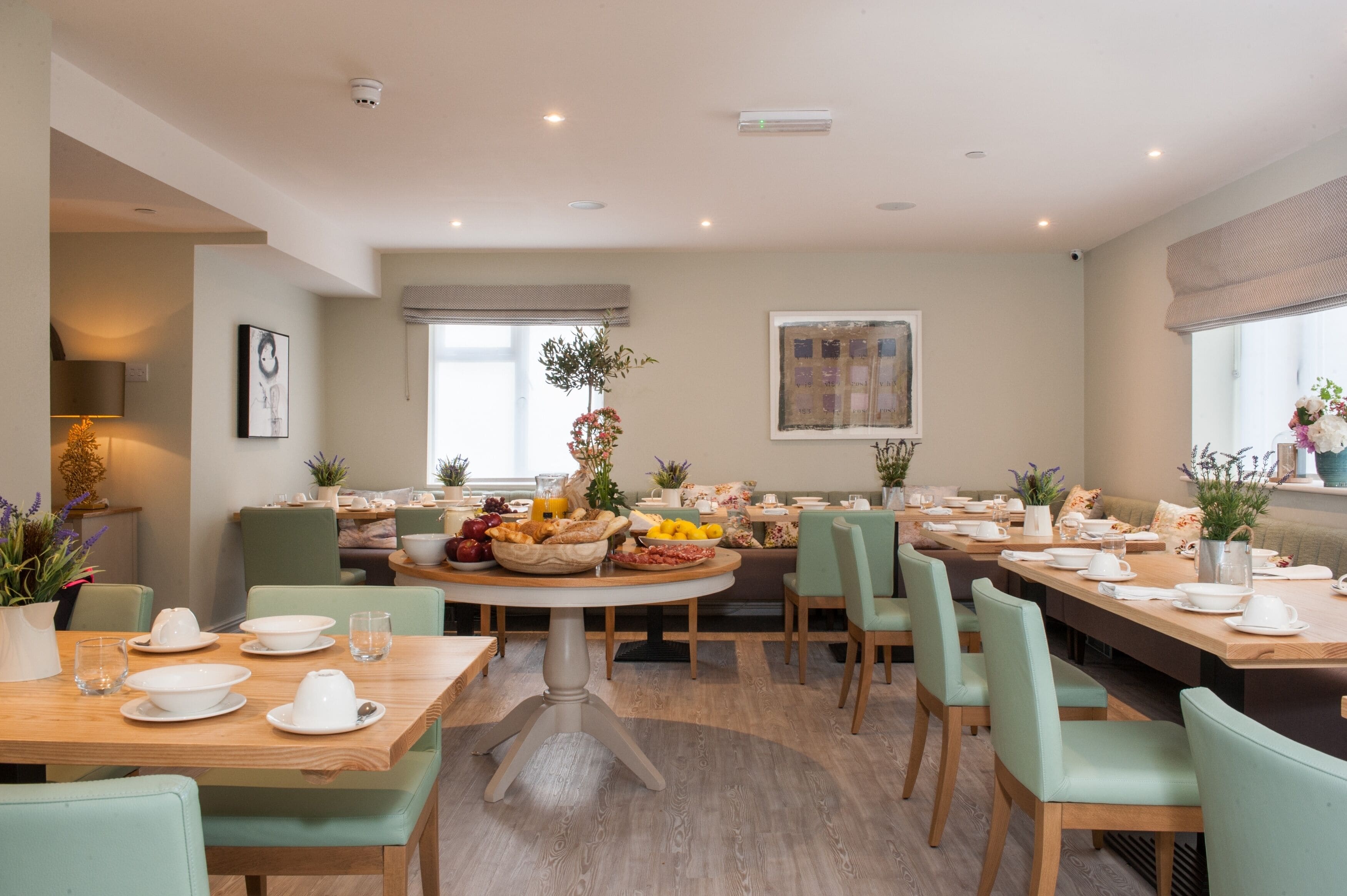A dining area with multiple tables set for meals, surrounded by green chairs.
