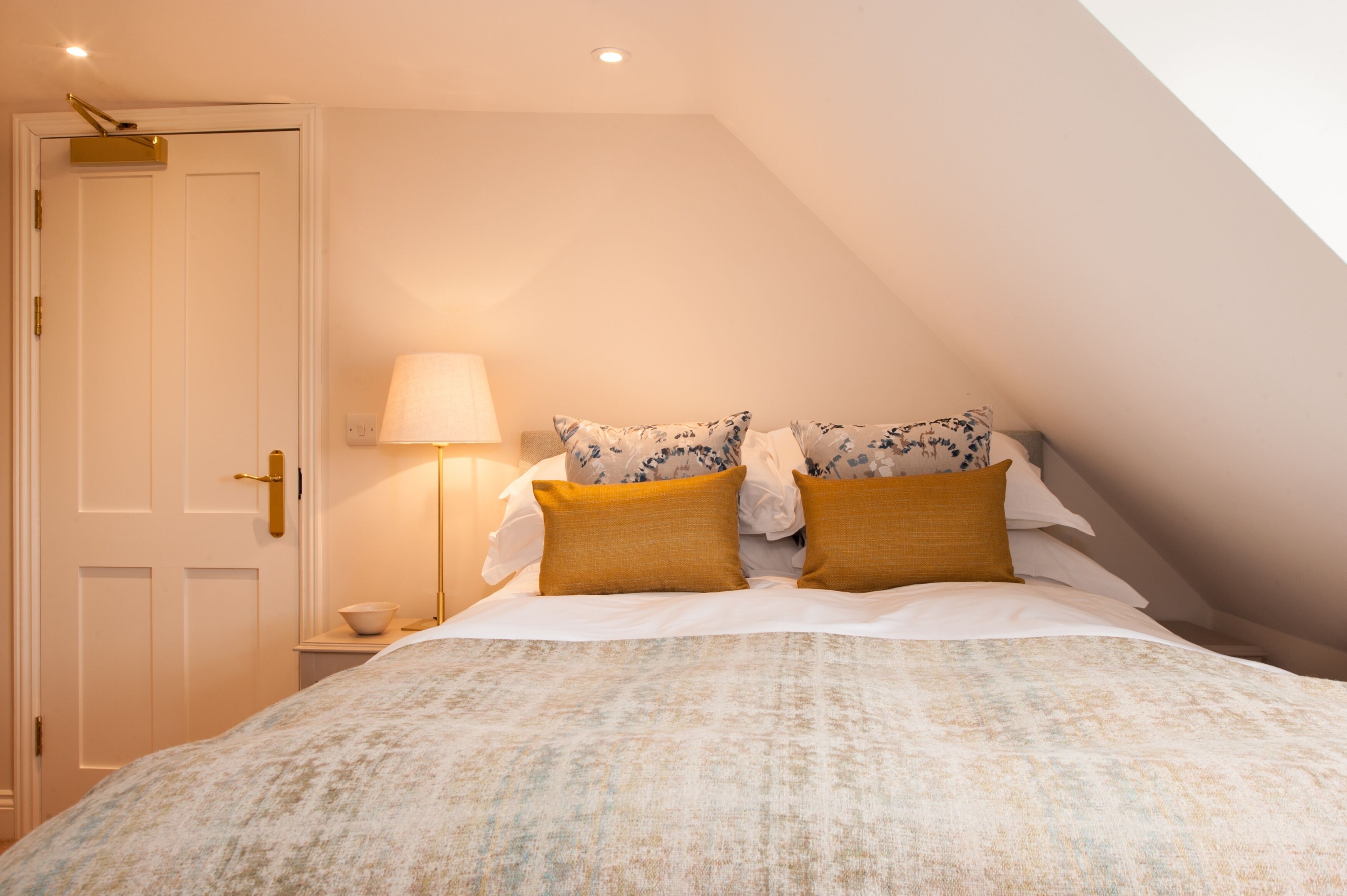 A bedroom with a bed, pillows, a nightstand, a lamp, and a door.