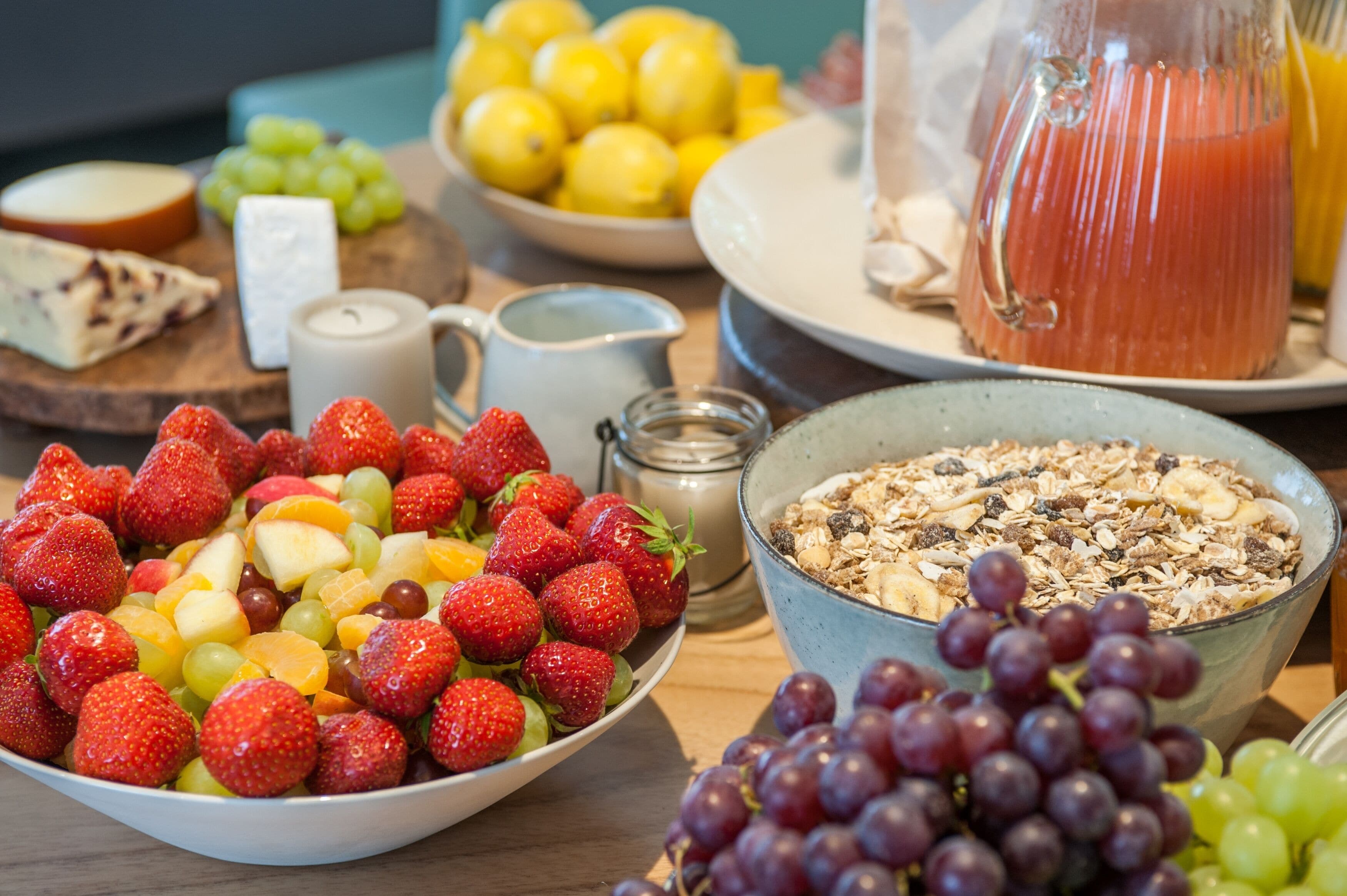 A breakfast table with various fruits, a pitcher of orange juice, and a bowl of cereal.