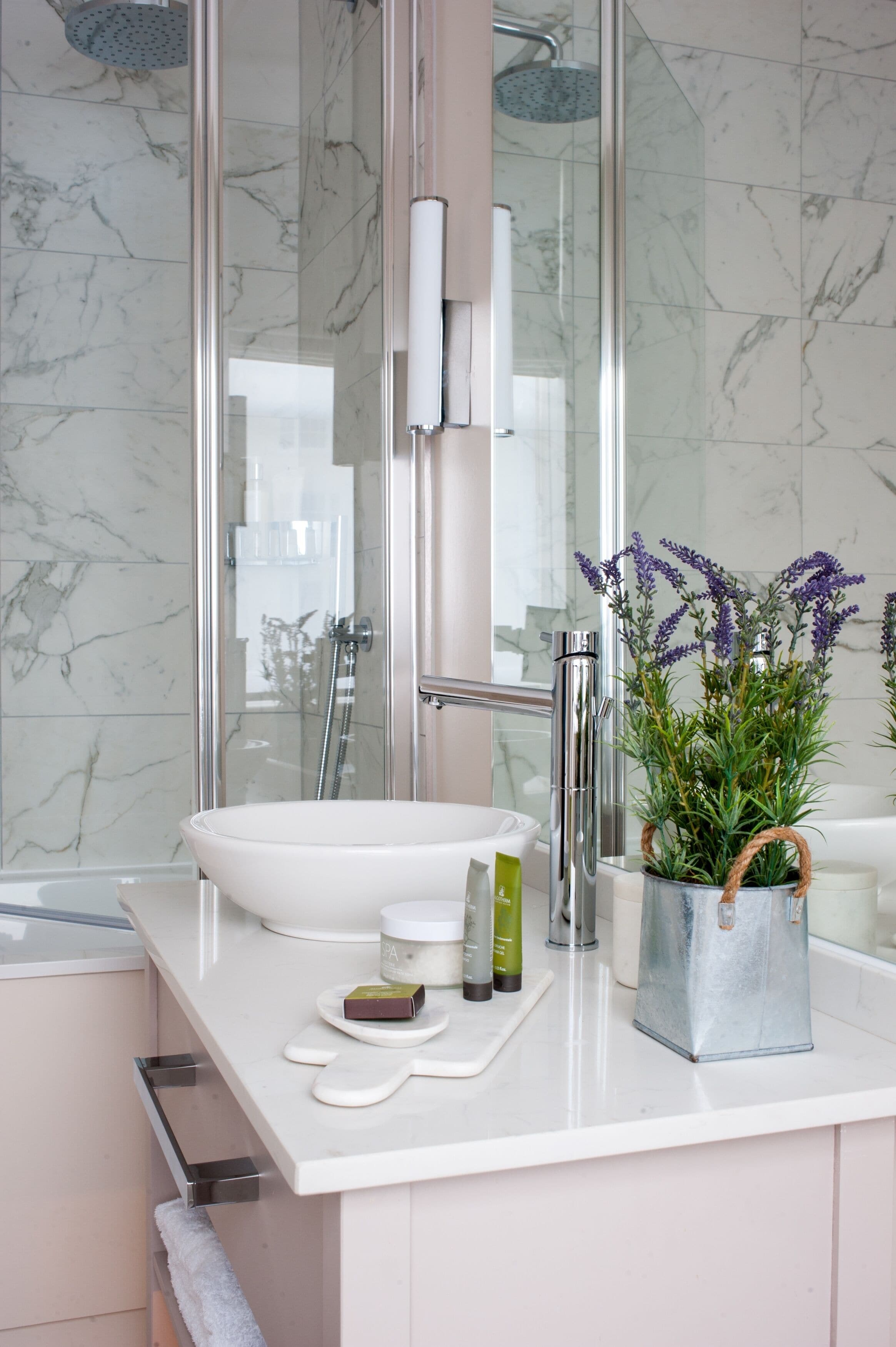 Une salle de bain moderne avec un grand miroir, un lavabo blanc, une douche et une plante en pot.