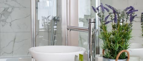 Ein modernes Badezimmer mit großem Spiegel, weißem Waschbecken, einer Dusche und einer Topfpflanze.