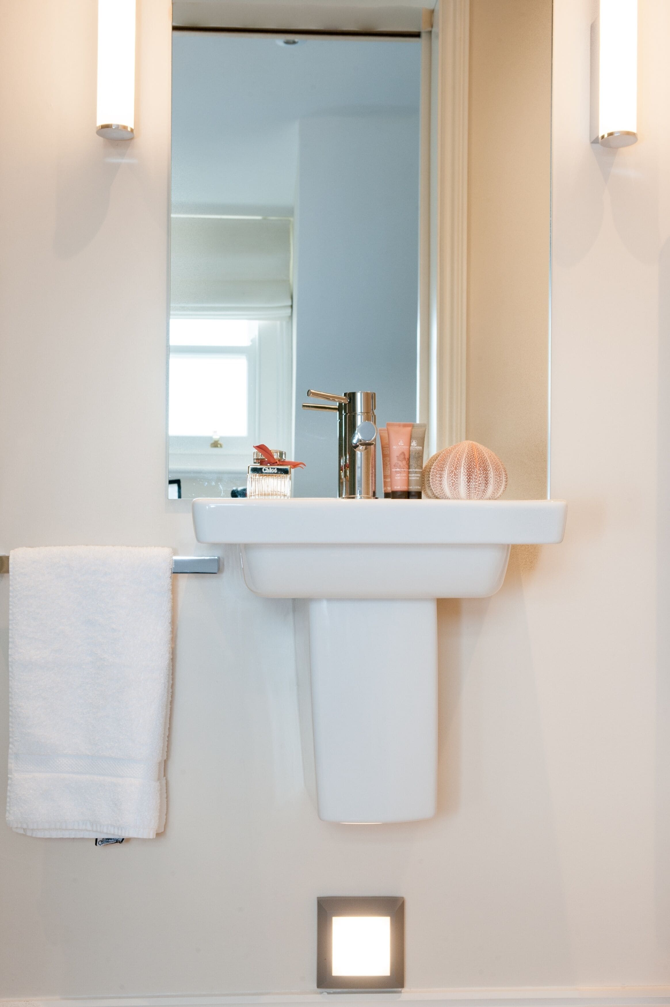 A bathroom with a white sink, a towel hanging on the wall, and a mirror above the sink.