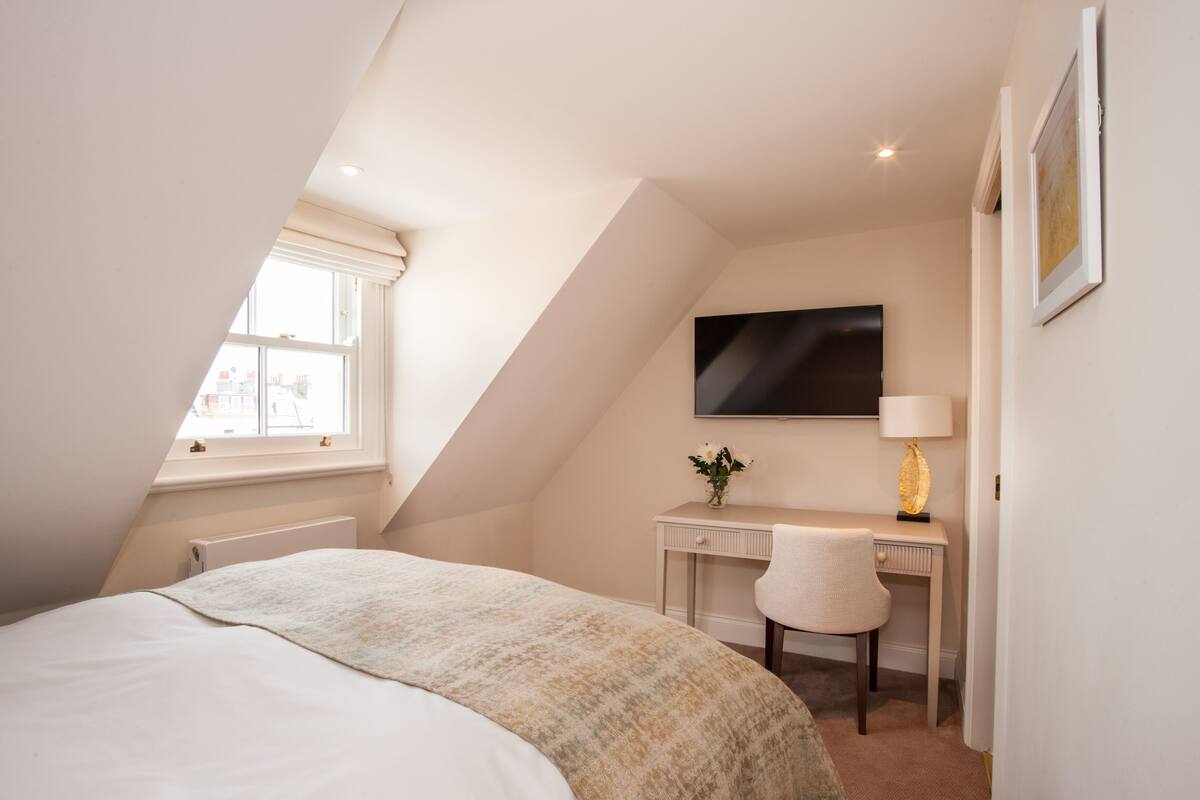 Een slaapkamer met een bed, een bureau, een stoel, een televisie en een raam.