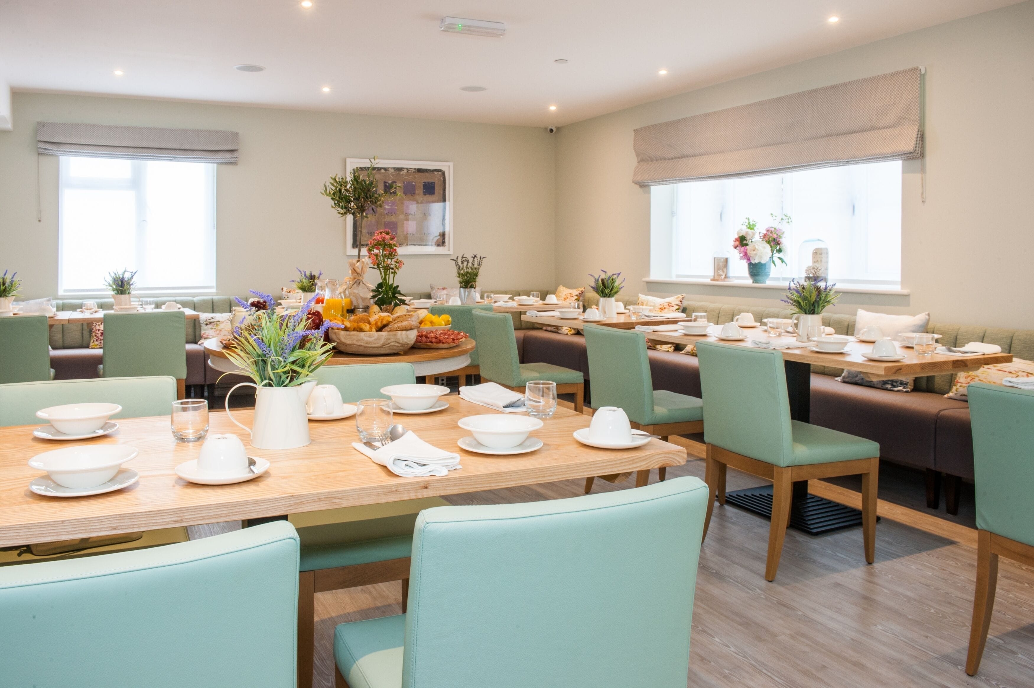 A dining area with multiple tables set for breakfast, featuring light green chairs, white tableware, and floral centerpieces.