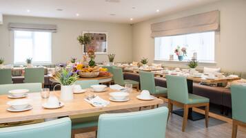 A dining area with multiple tables set for breakfast, featuring light green chairs, white tableware, and floral centerpieces.