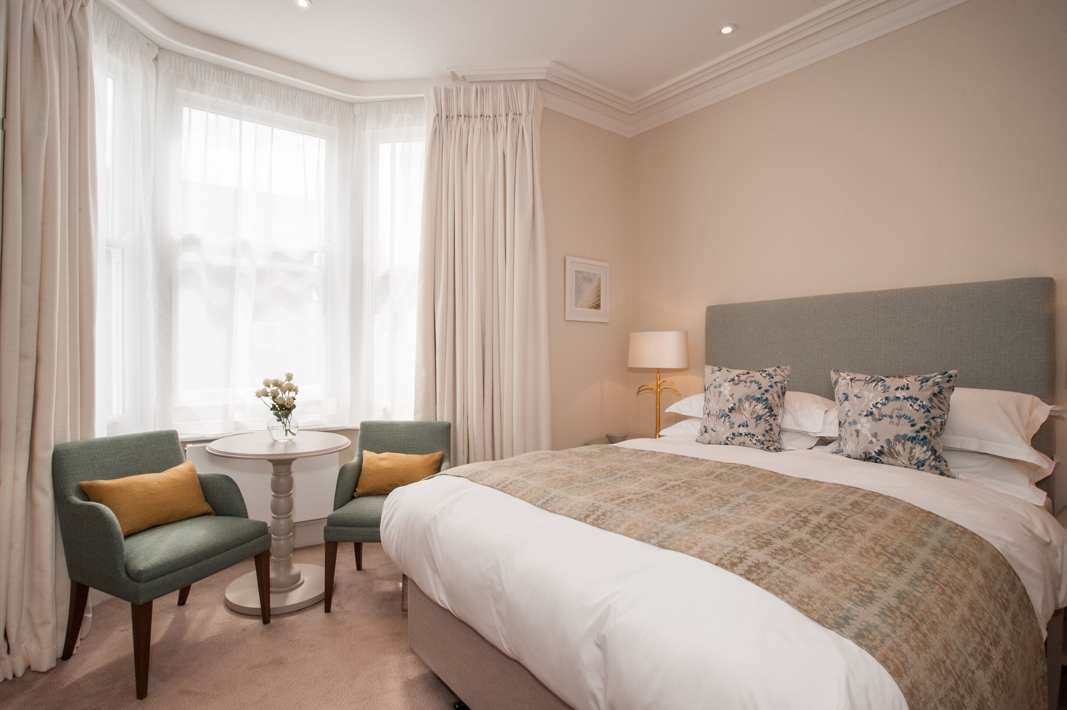 A hotel room with a large bed, two armchairs, a small round table, and a lamp.