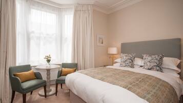 A hotel room with a large bed, two armchairs, a small round table, and a lamp.