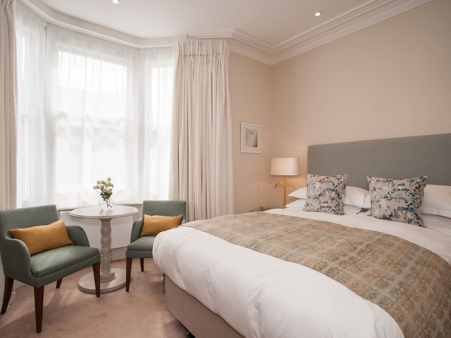 A hotel room with a large bed, two armchairs, a small round table, and a lamp.
