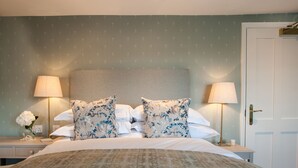 Una cama bien hecha con almohadas florales, dos lámparas de noche y una mesita con un florero.