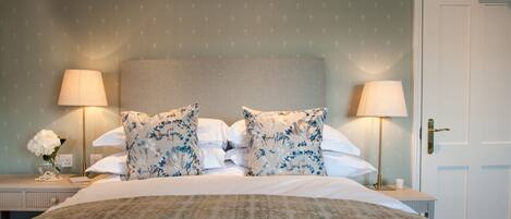 A neatly made bed with floral pillows, two bedside lamps, and a small table with a vase of flowers.