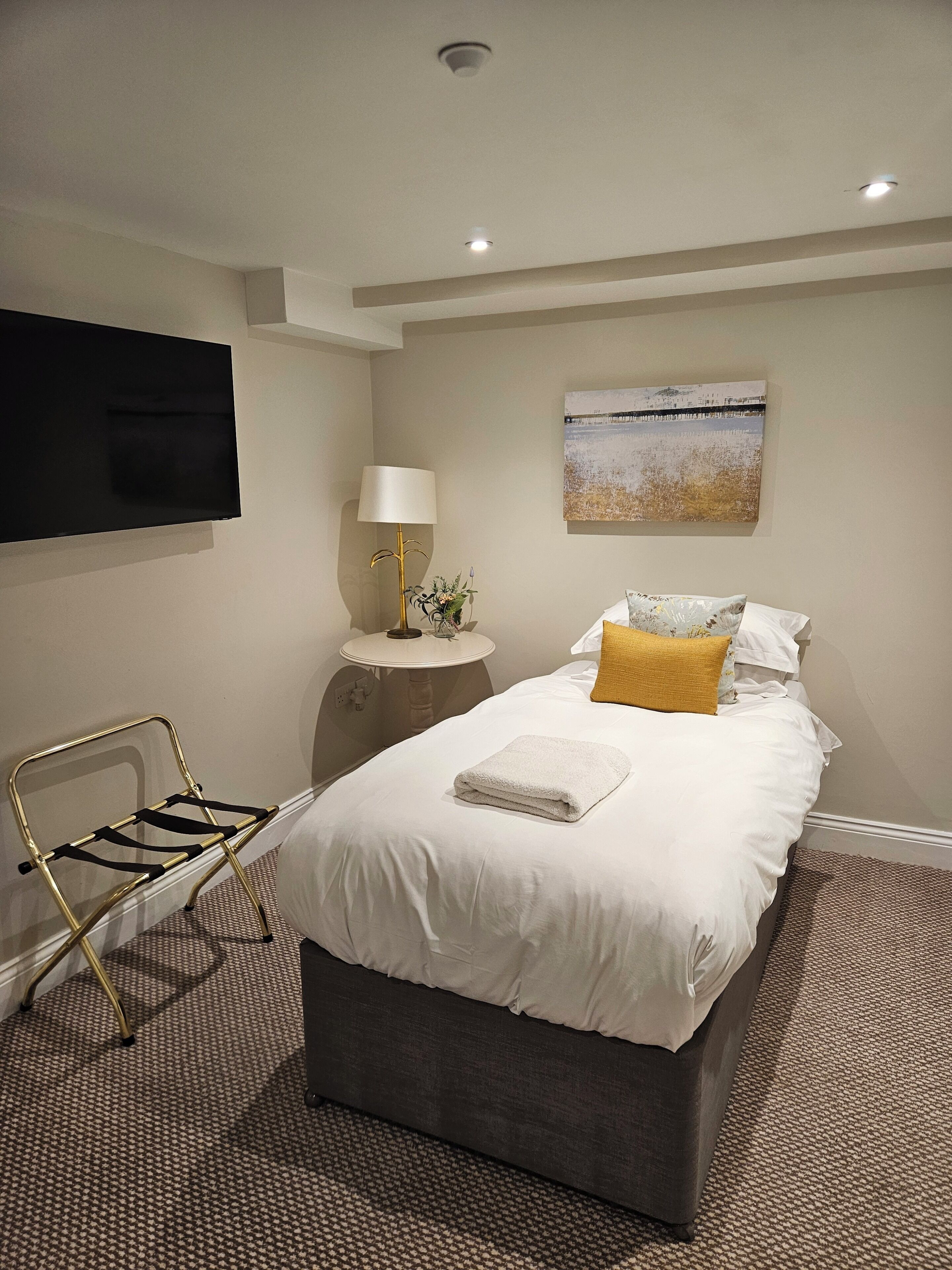 A hotel room with a bed, a bedside table, a lamp, a TV, and a chair.