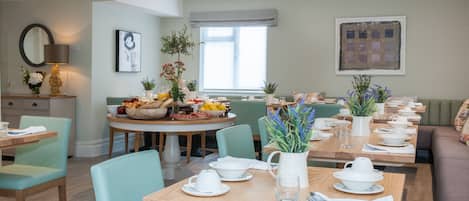 A dining area with multiple tables set for meals, chairs, and a sofa.
