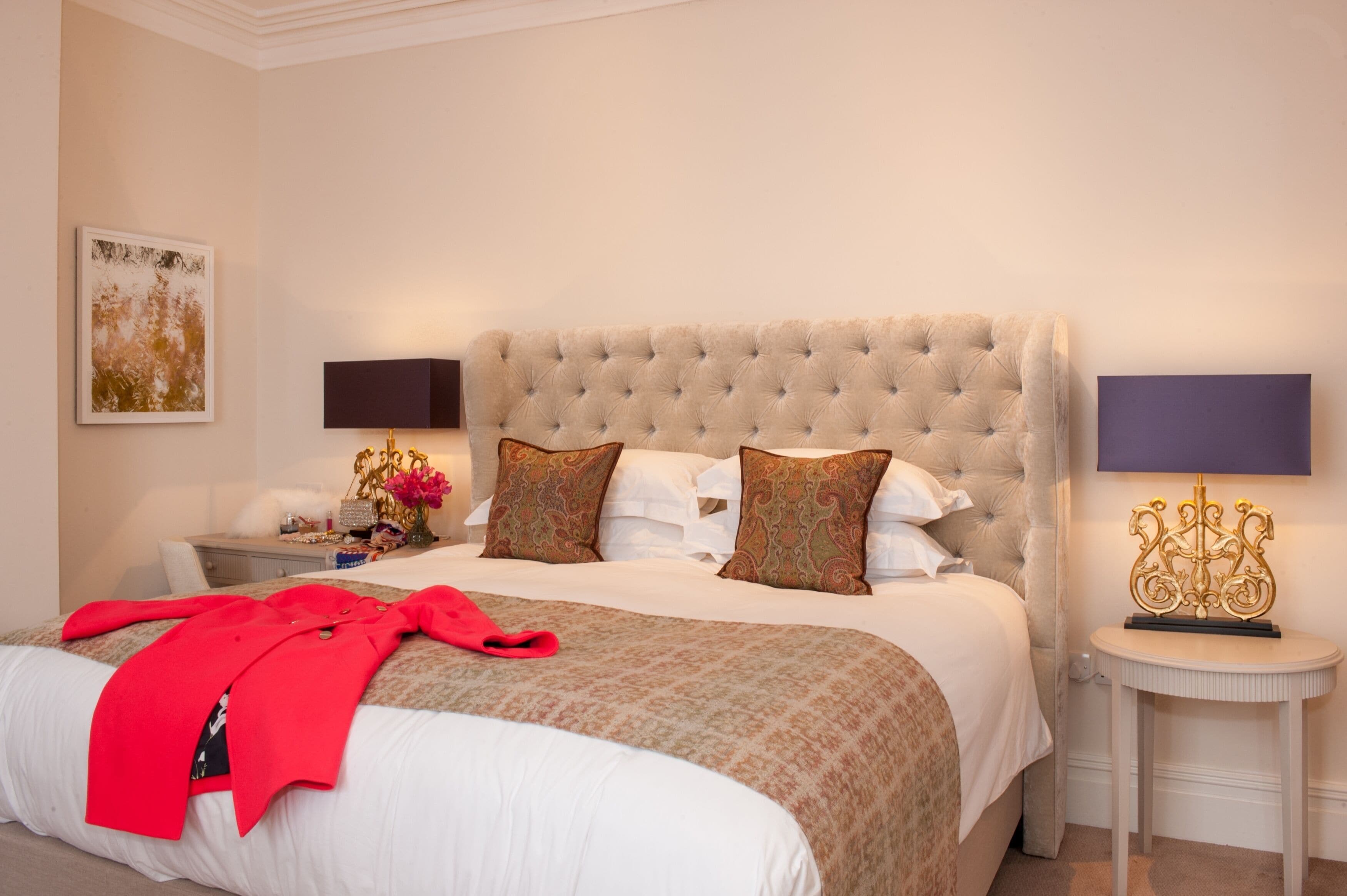 A neatly made bed with a red blanket, a tufted headboard, and two bedside tables with lamps.