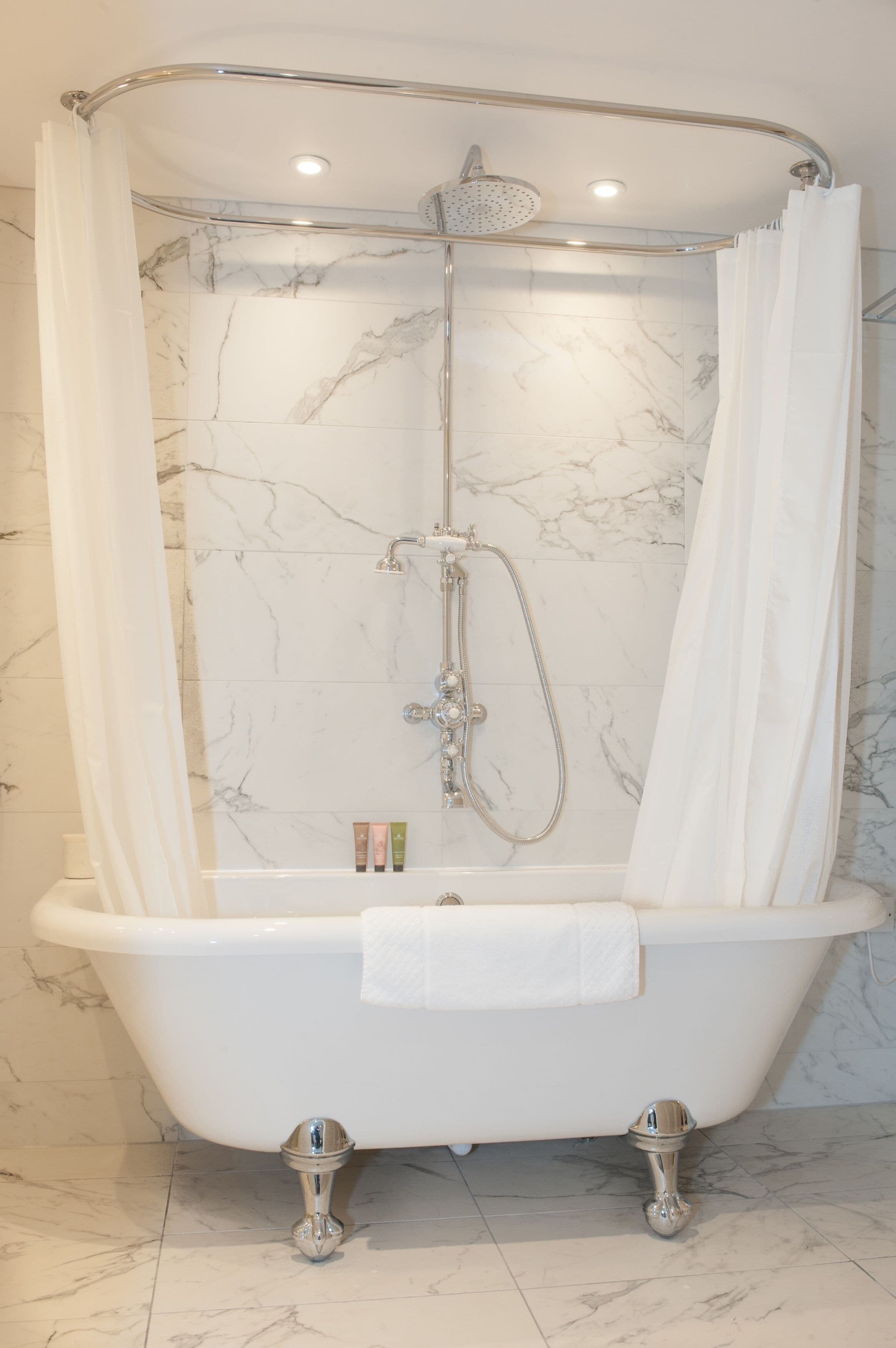A clawfoot bathtub with a showerhead and curtain in a bathroom with marble walls.