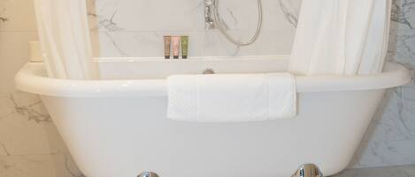 A clawfoot bathtub with a showerhead and curtain in a bathroom with marble walls.