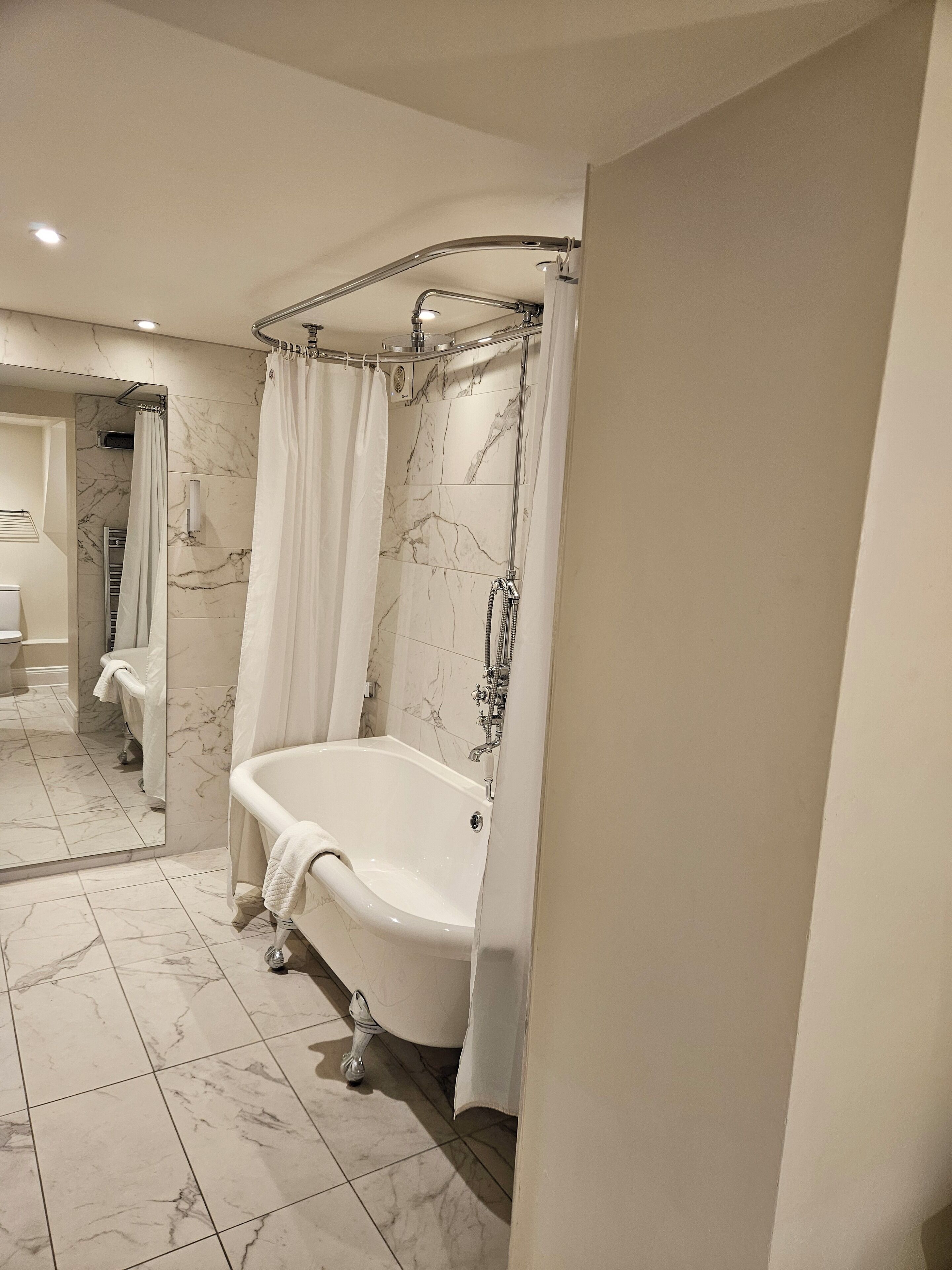 Un baño con una bañera independiente, una ducha con puerta de vidrio y pisos de mármol.