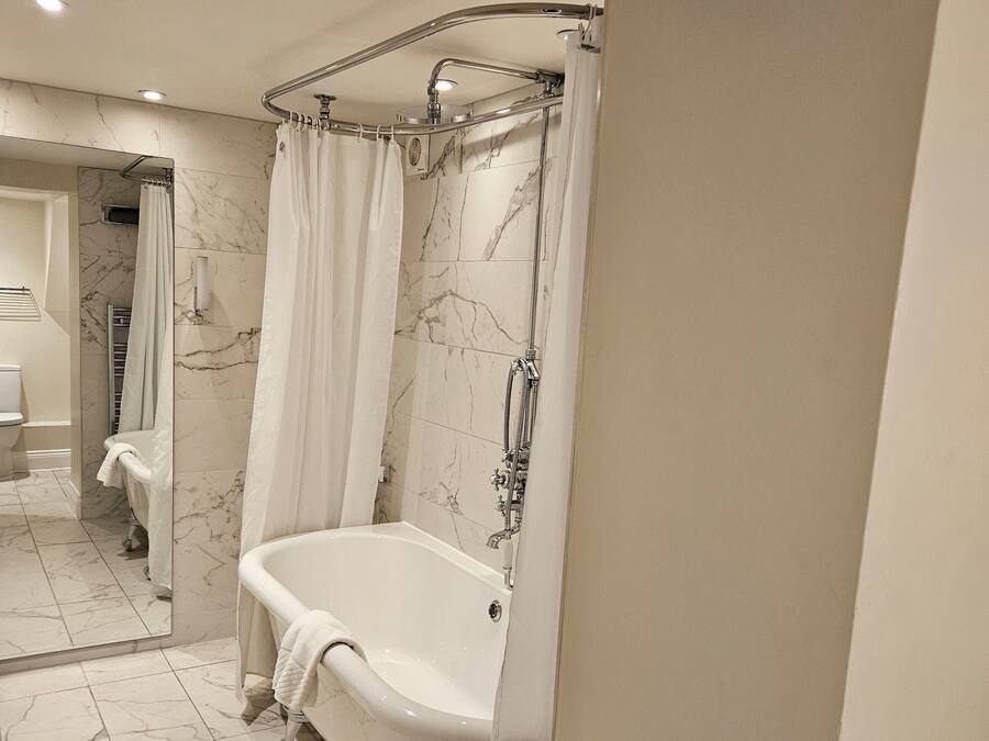 Un baño con una bañera independiente, una ducha con puerta de vidrio y pisos de mármol.